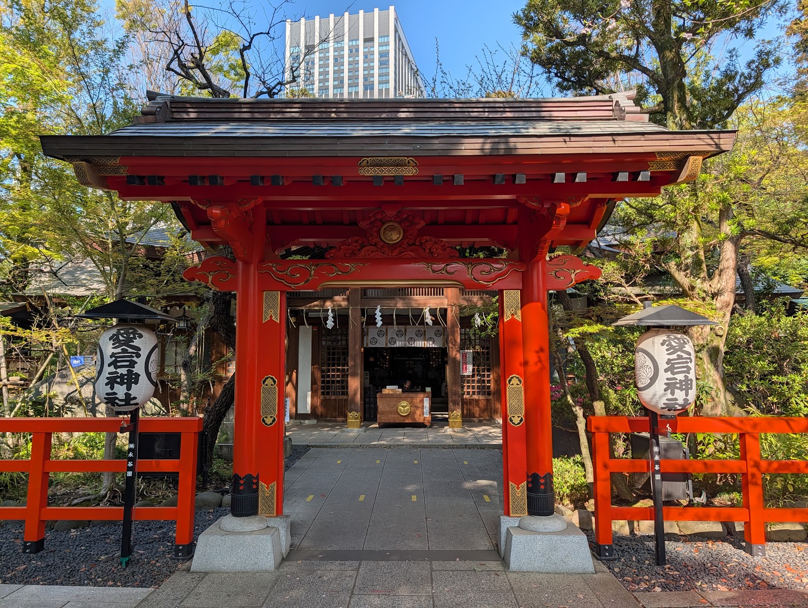 愛宕神社の朱の楼門。両脇の提灯に愛宕神社の文字、奥に拝殿と賽銭箱、上に高層ビル。