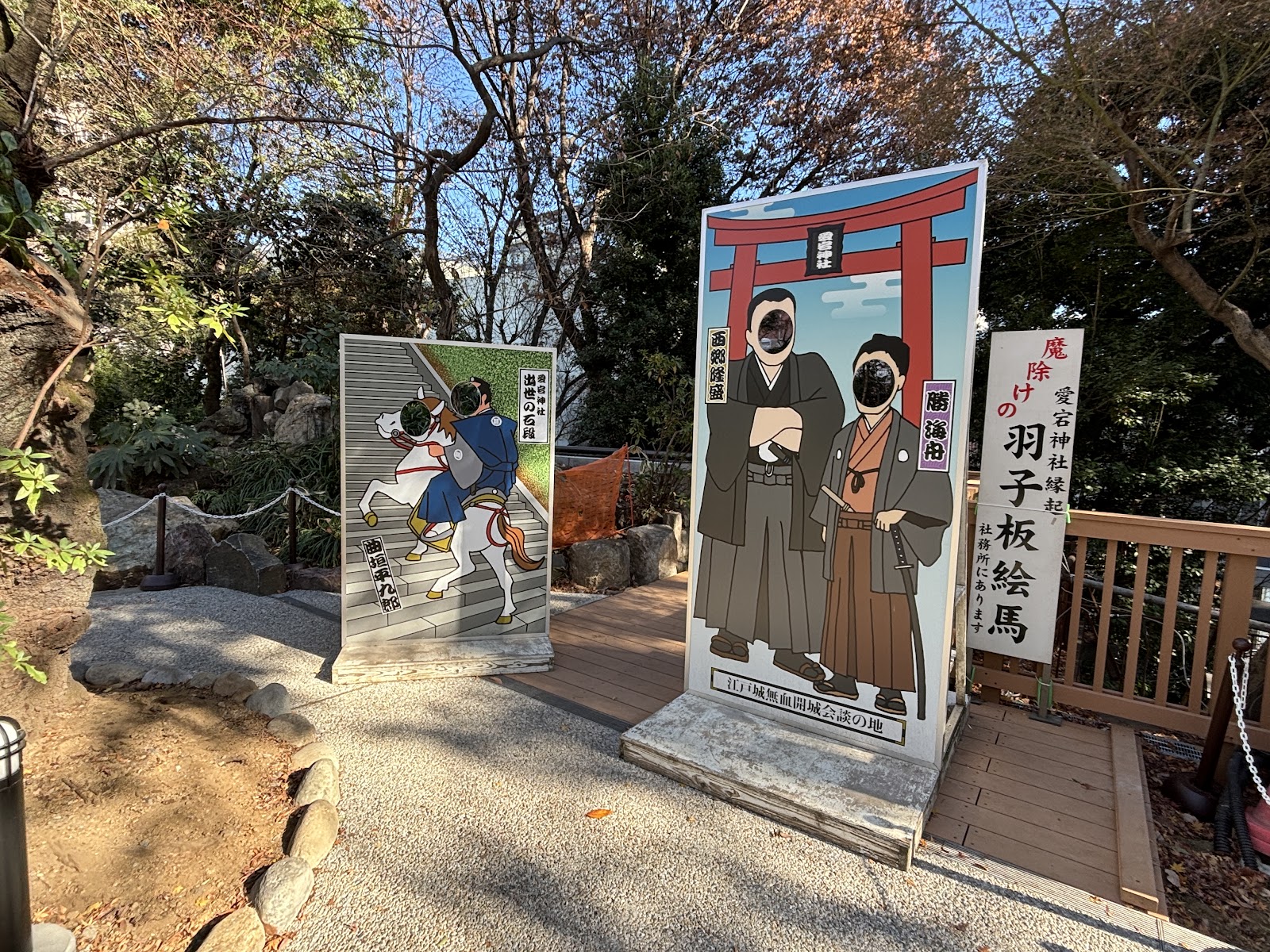 木の甲板に立つ二枚の顔出し看板。石段を馬で駆ける絵と、鳥居の前に立つ二人の絵。